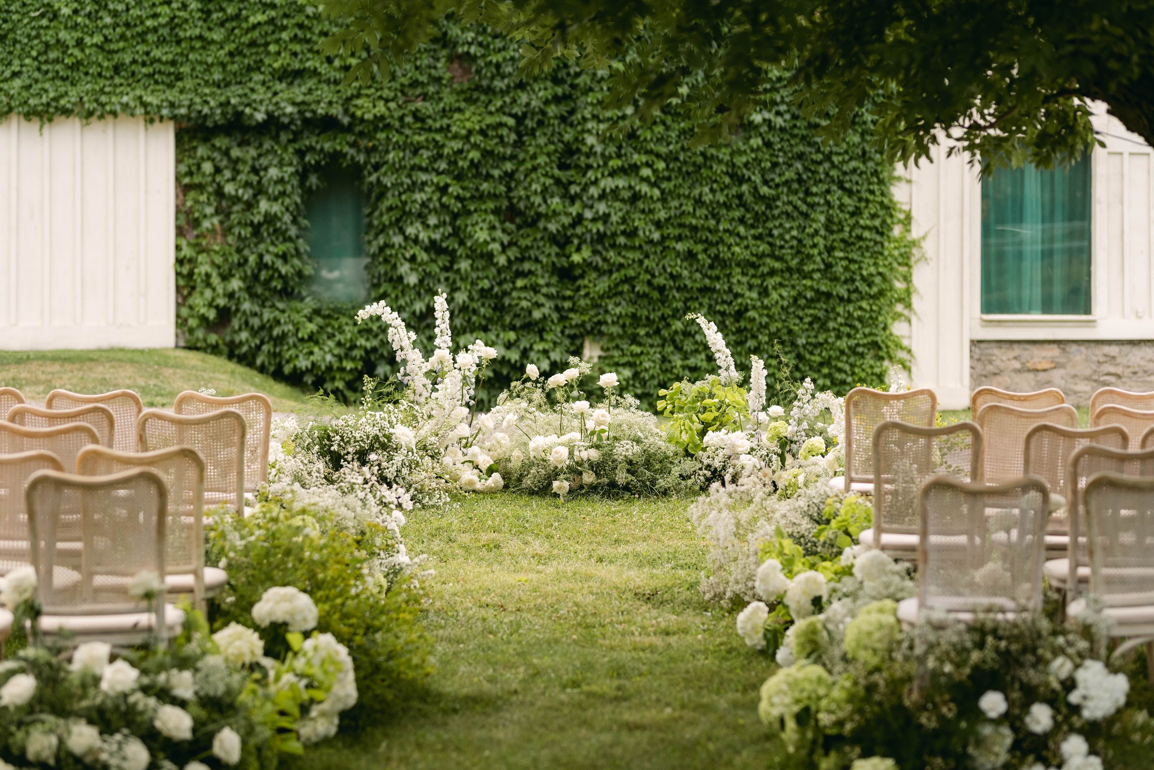 The 1881 Barn at Sorella — ivy-covered wall with white floral aisle arrangements and cane ceremony chairs