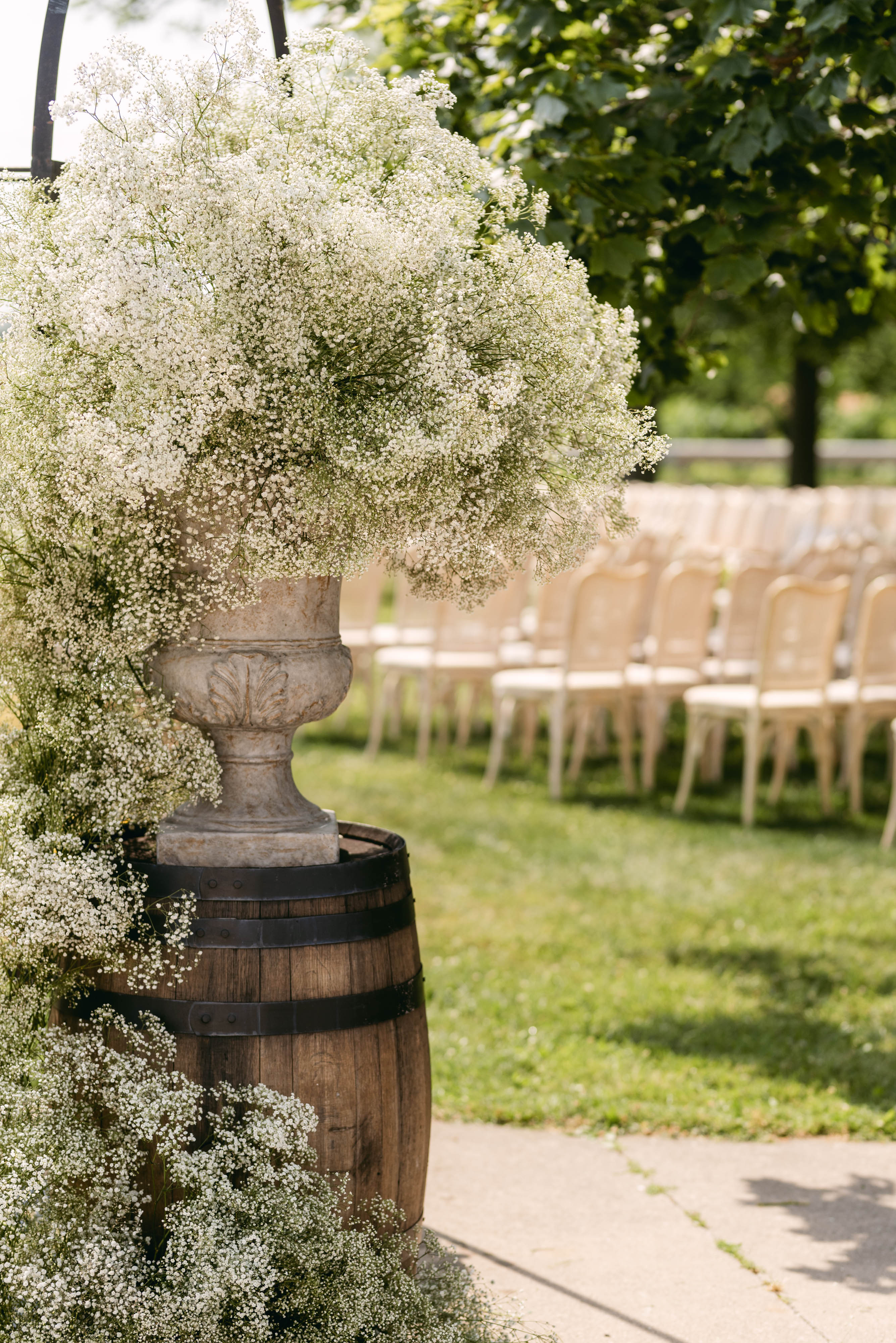Wine barrel with a stone urn overflowing with baby's breath at the ceremony aisle entrance