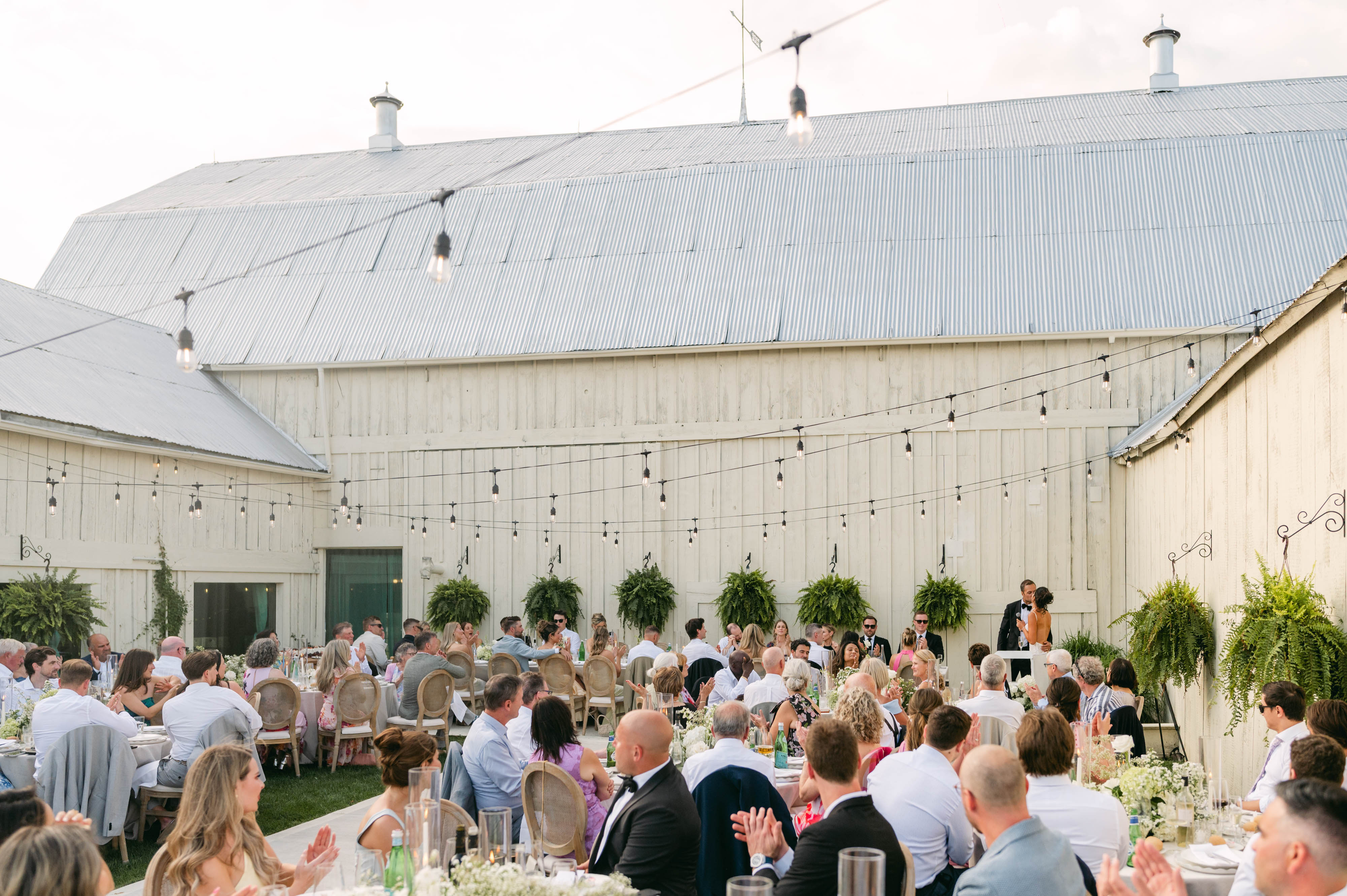 Guests seated for dinner in the courtyard reception under string lights and the 1881 barn