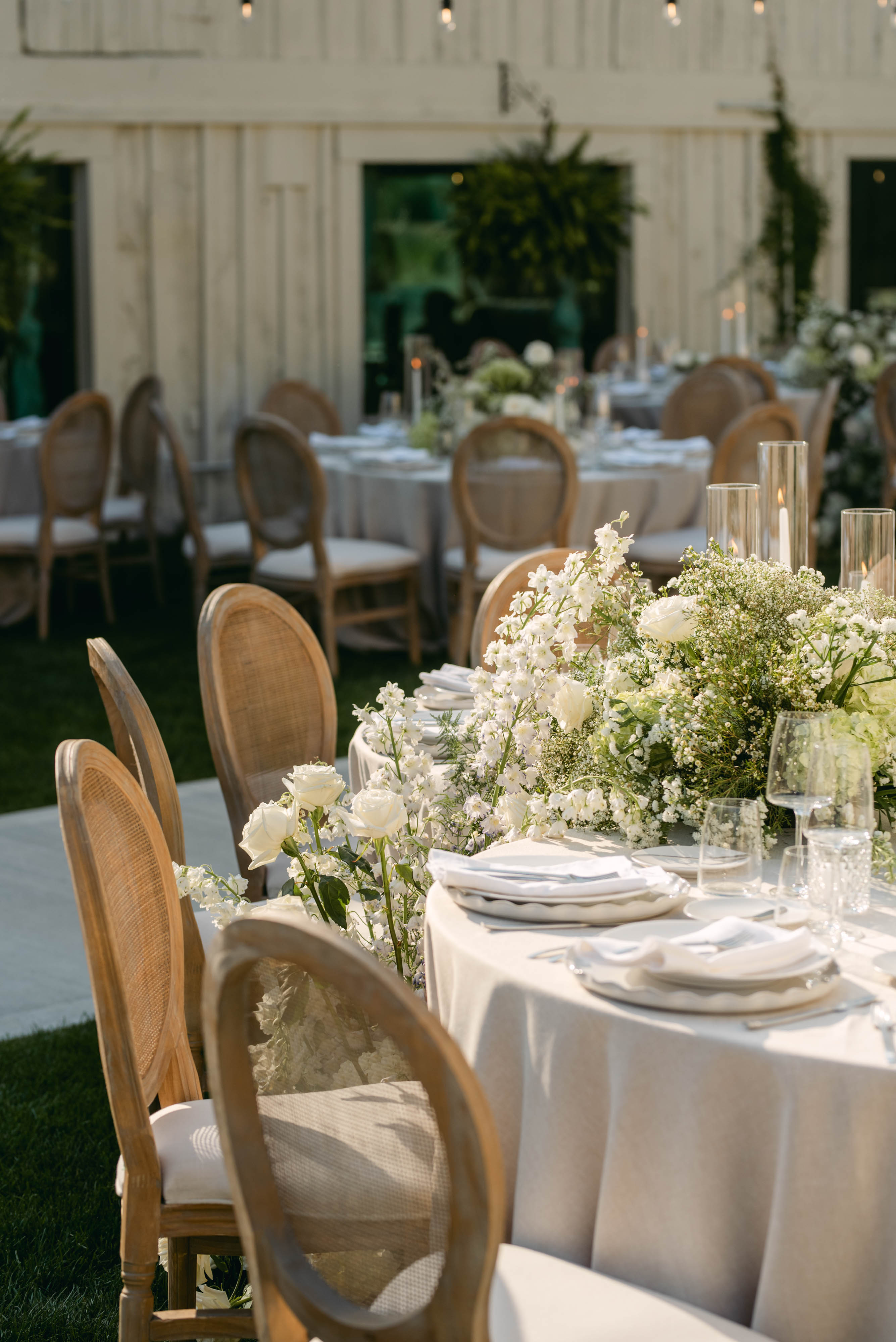 Wedding tablescape at Sorella 1881 — cascading white florals, taper candles, and cane chairs against the barn