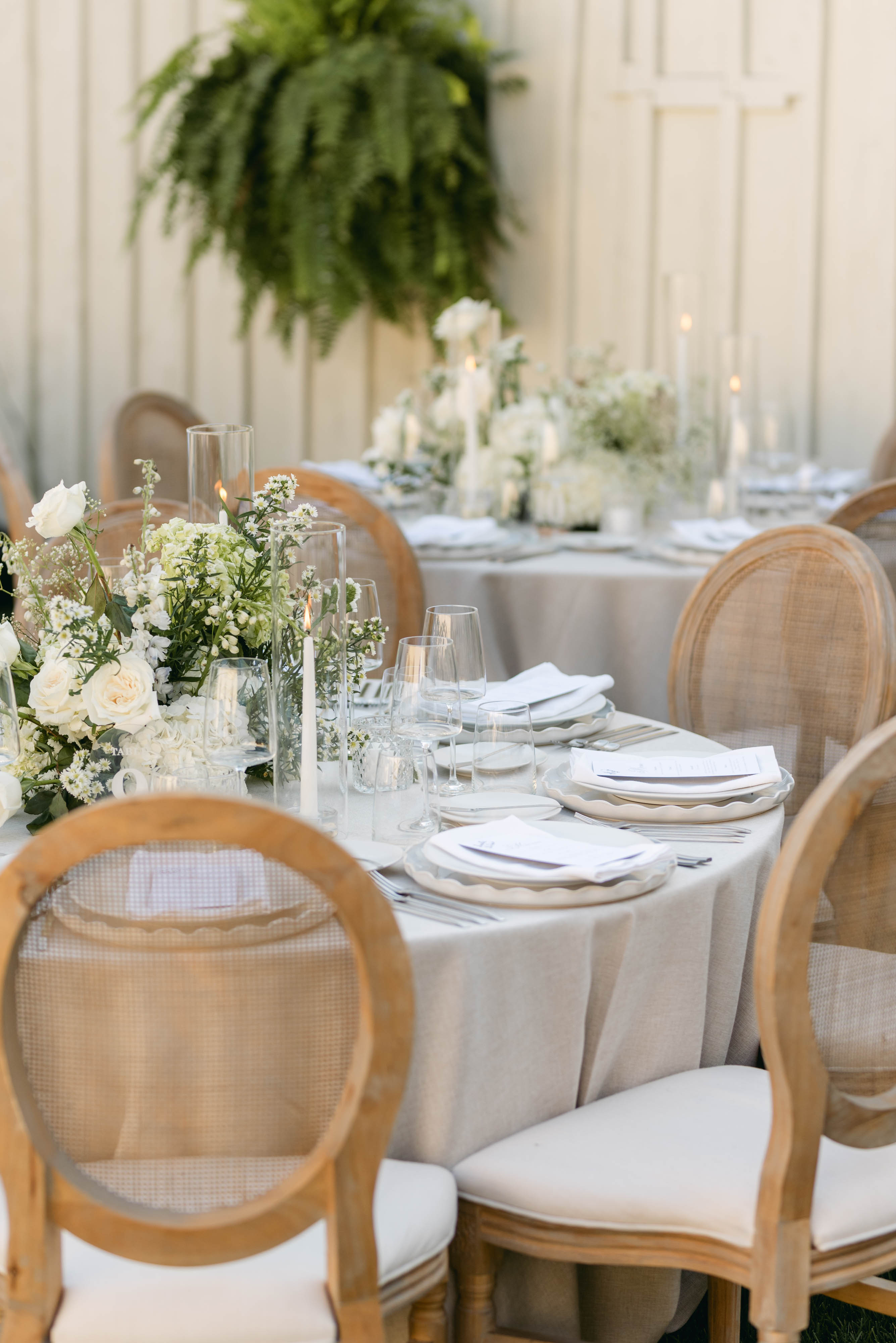 Reception table set with white florals and taper candles beside a hanging fern at the barn