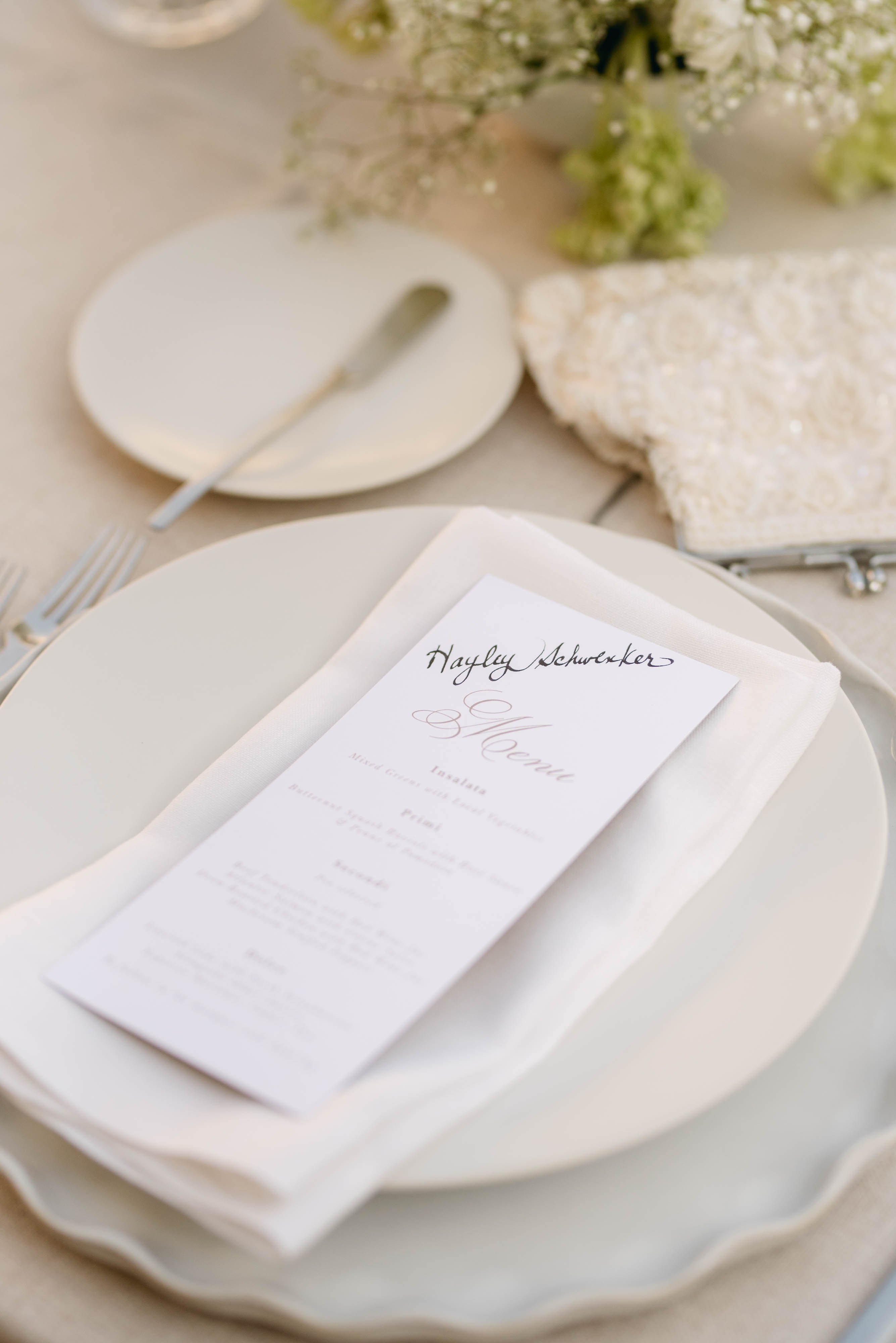 Handwritten menu place setting on scalloped charger plate with white florals at Sorella 1881