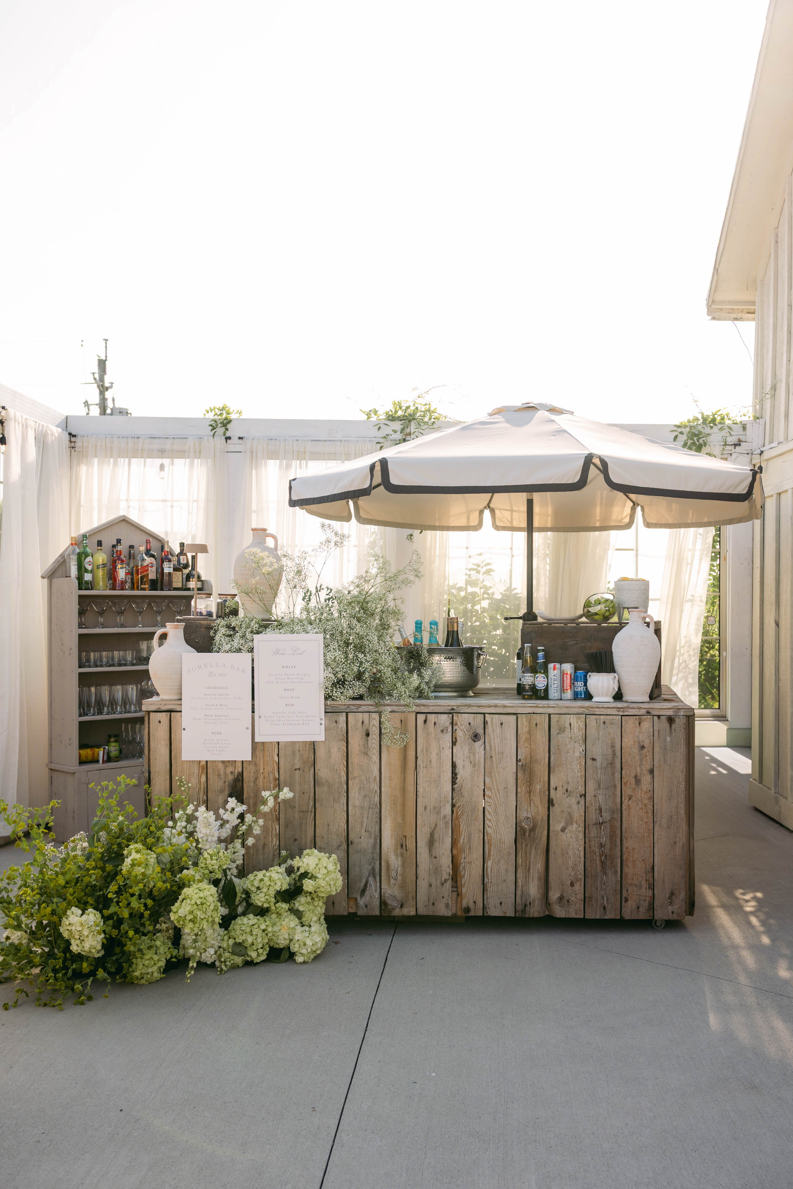 Rustic wooden bar with cream umbrella and floral arrangement at Sorella 1881