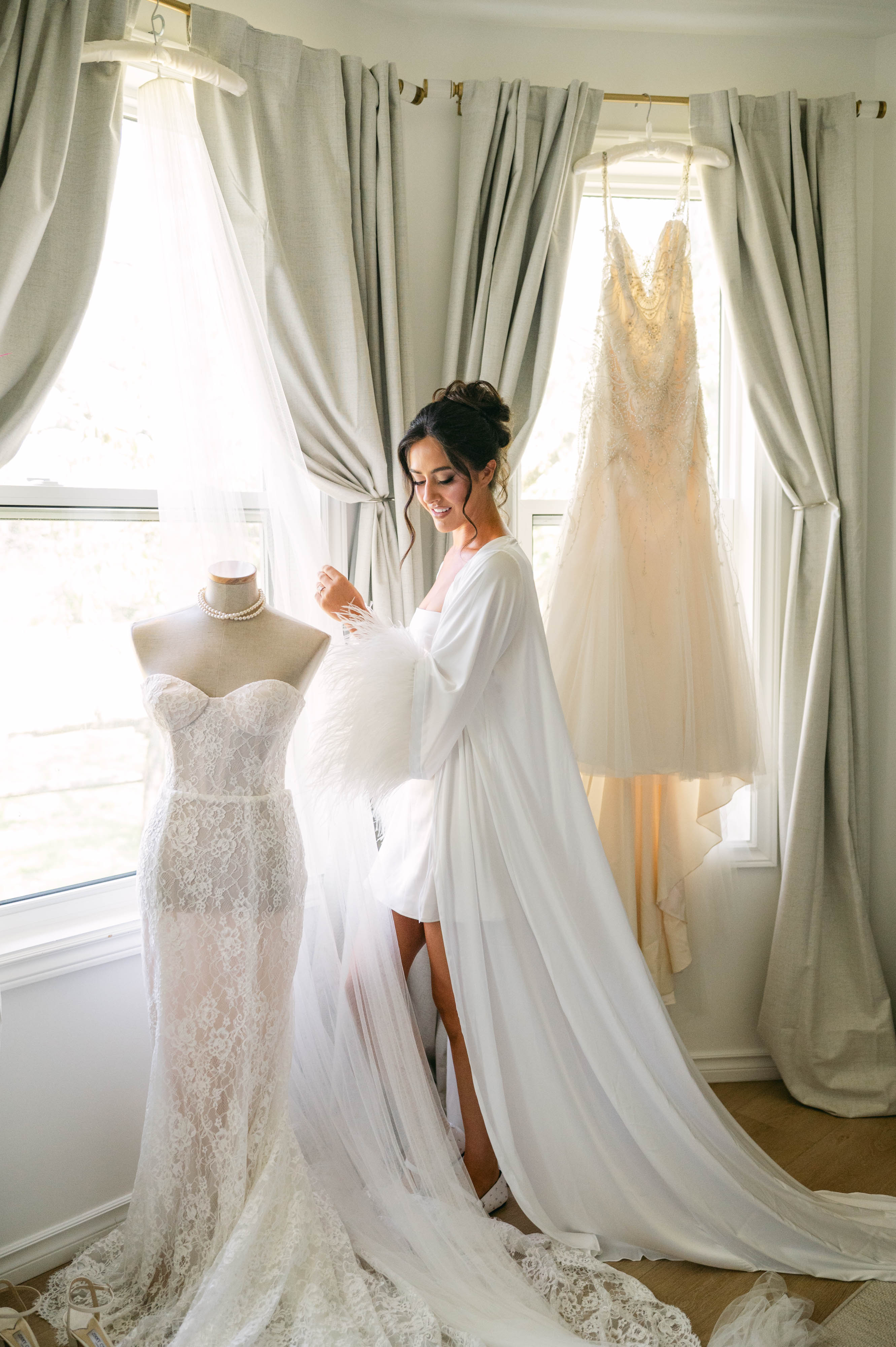 Bride in white robe styling her feathered dress in the Ranch House getting-ready suite at Sorella 1881