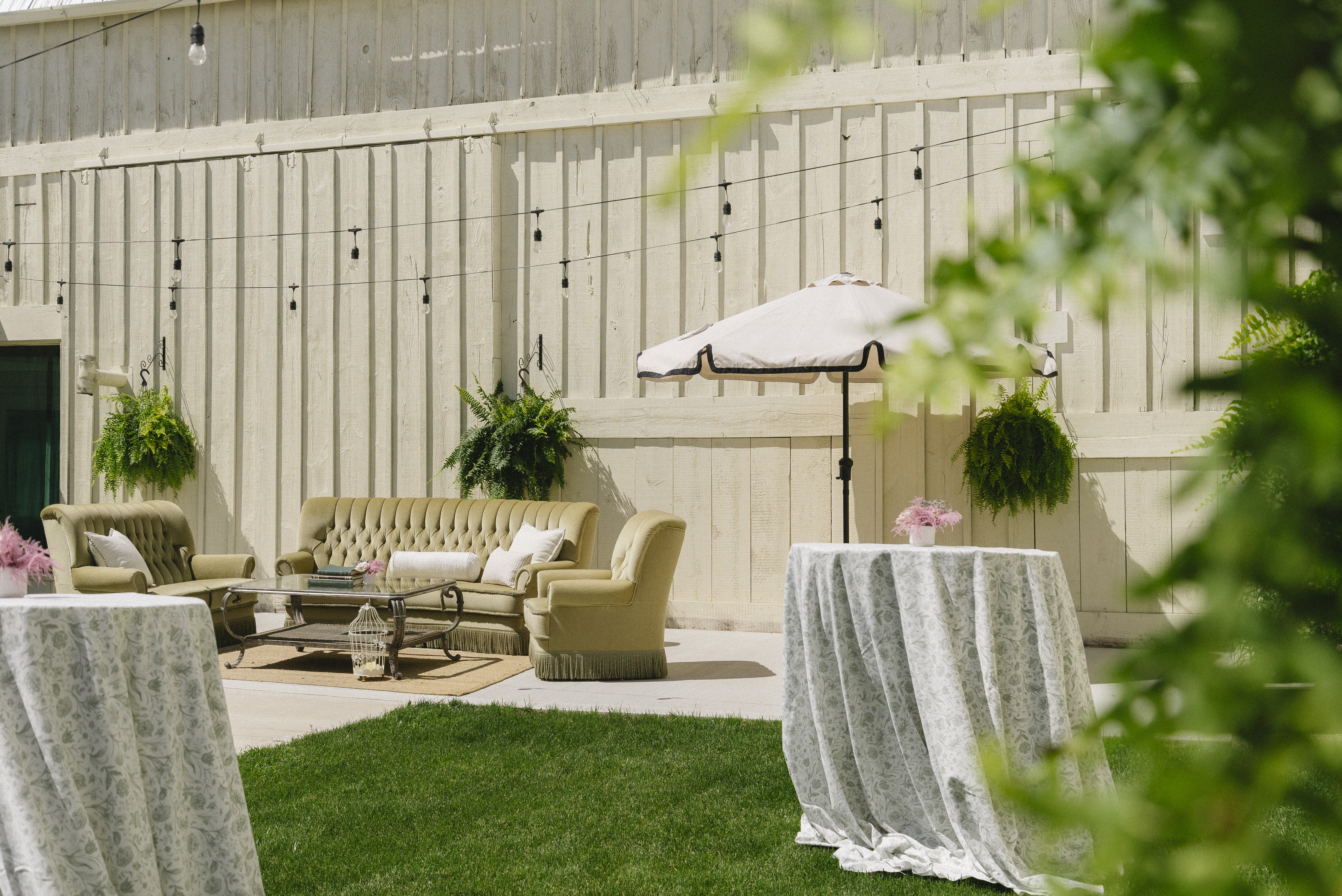 Estate cocktail lounge — vintage tan sofas and umbrella-shaded bistro tables against the barn wall