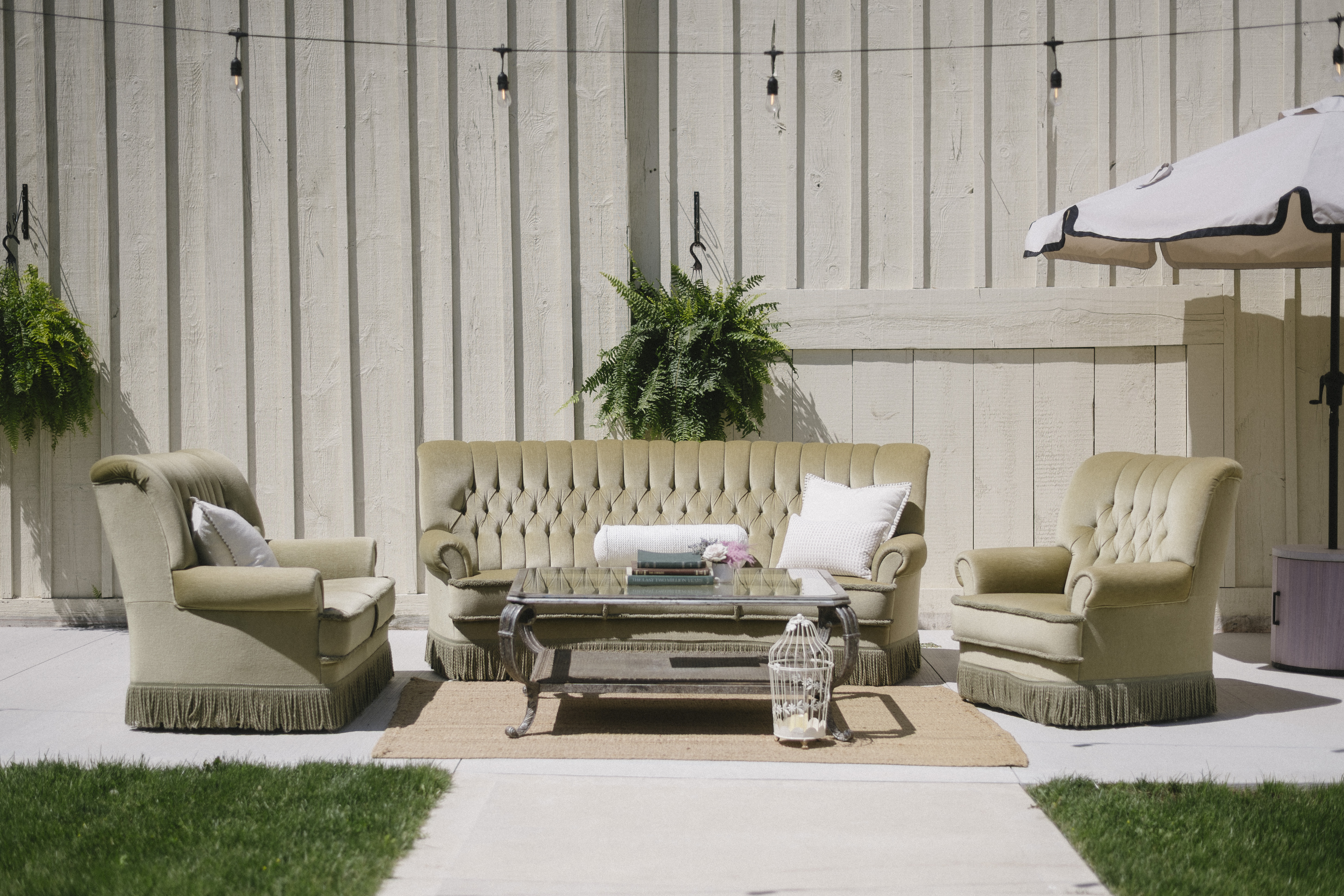 Outdoor lounge arrangement with green tufted sofas and armchairs beneath string lights at Sorella 1881