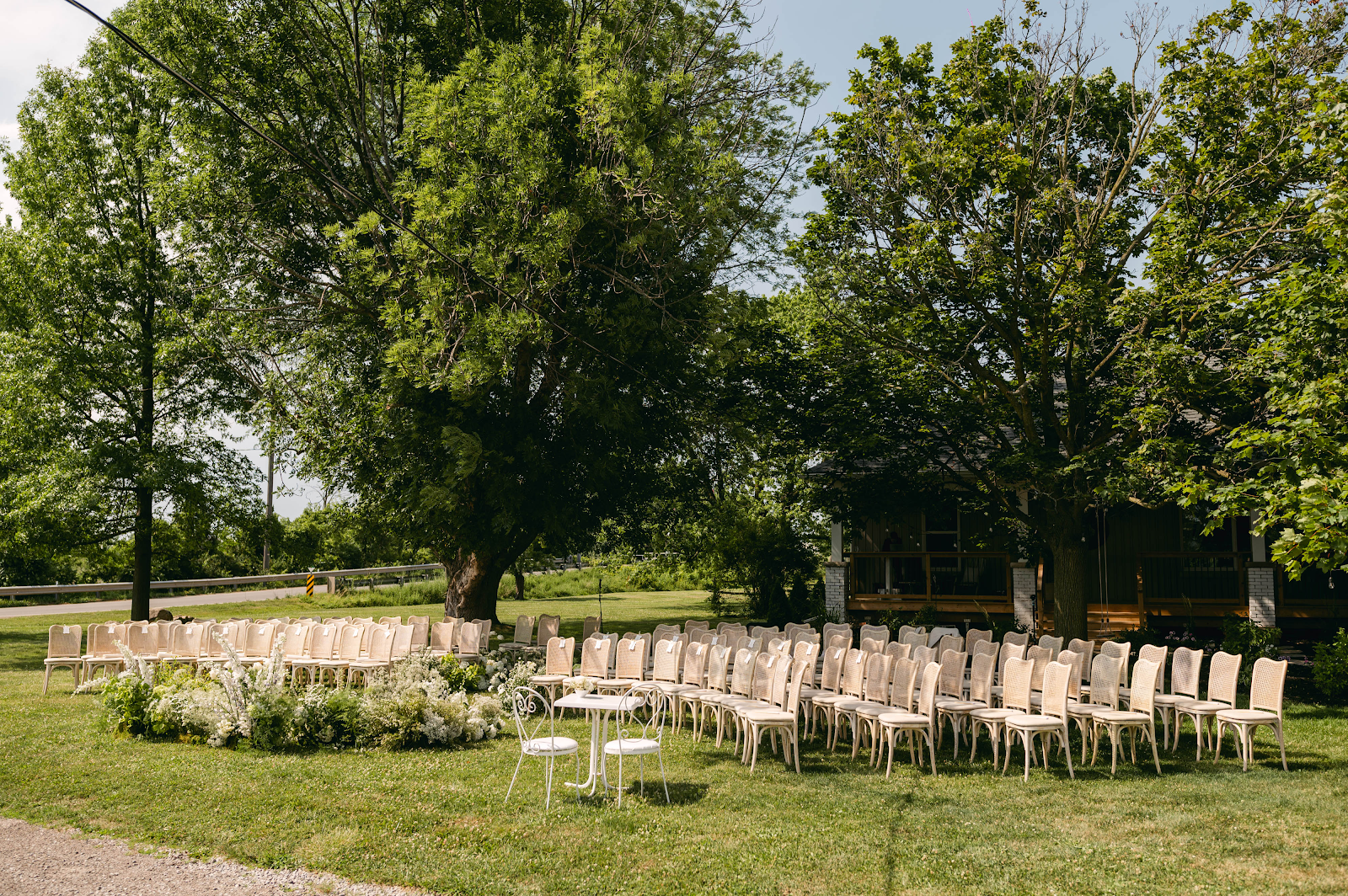 Outdoor ceremony setup beneath mature trees at Sorella 1881 — rows of cream chairs on lawn