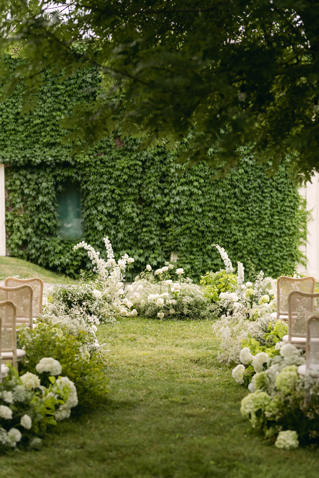 Ivy-covered barn ceremony aisle with white hydrangeas and rattan chairs at Sorella 1881